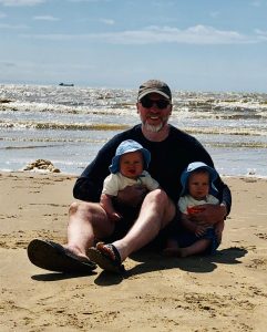 Mark parsons sitting on a beach with his two twins in his lap