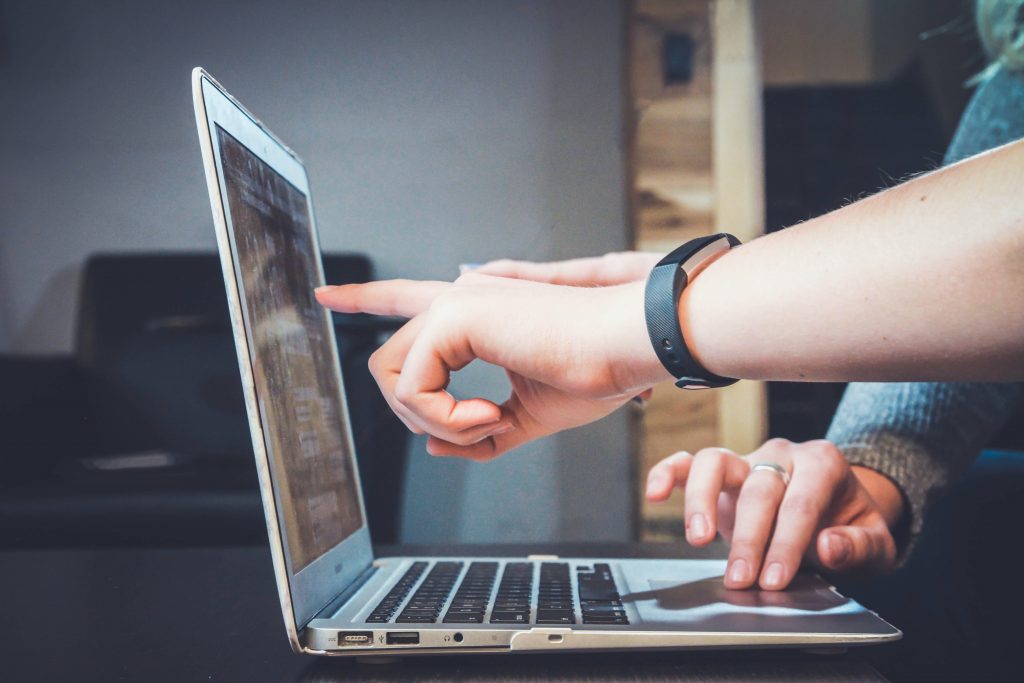 A side on image of a laptop on a desk with a person pointing at the screen